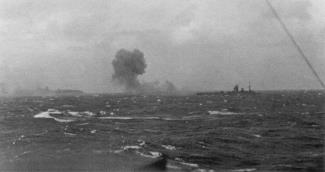 HMS Rodney firing on Bismarck, seen burning in the distance